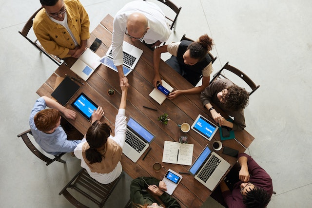 An overhead view of several property managers sitting at a large wooden table with various electronics and notebooks plan a management strategy for a property investor